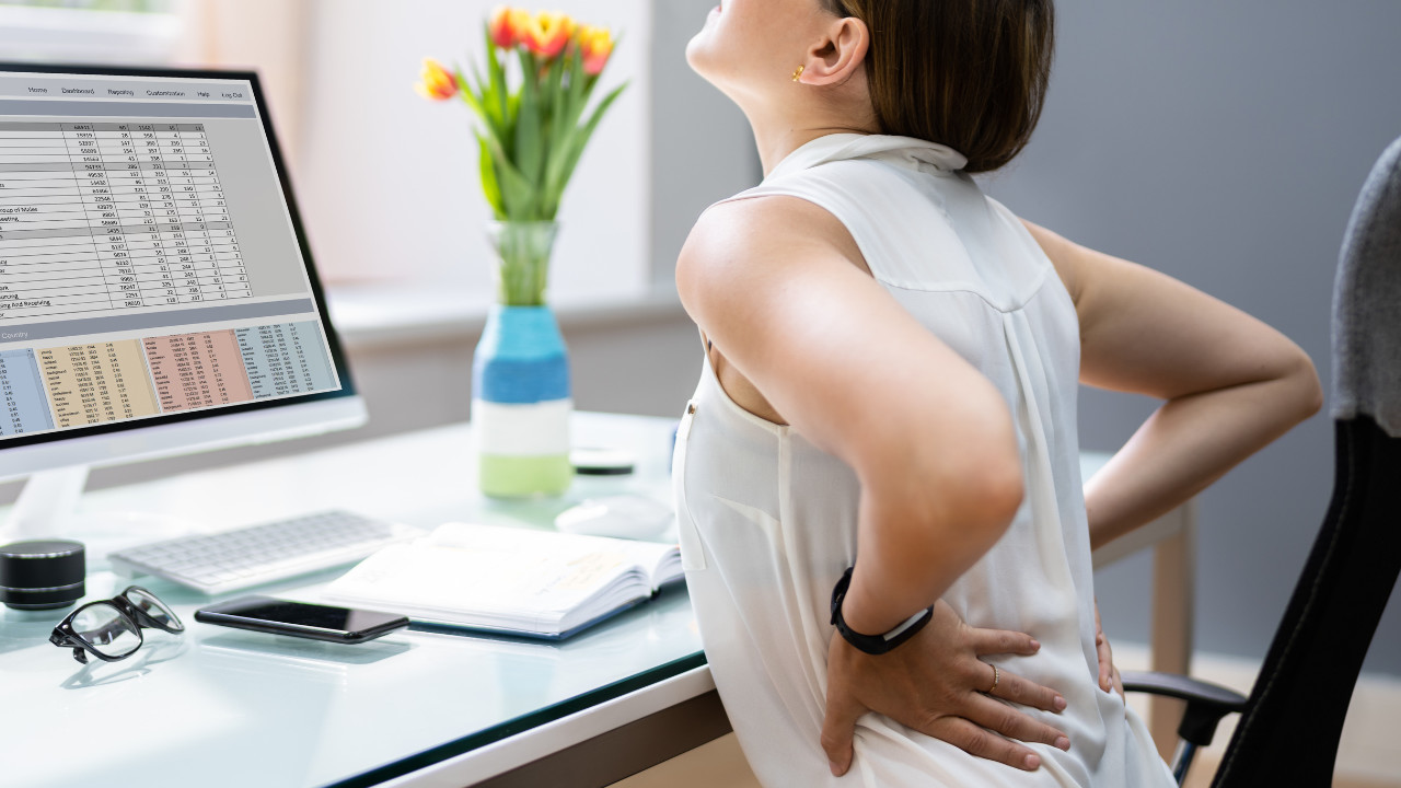 picture of woman sitting at desk holding her painful lower back